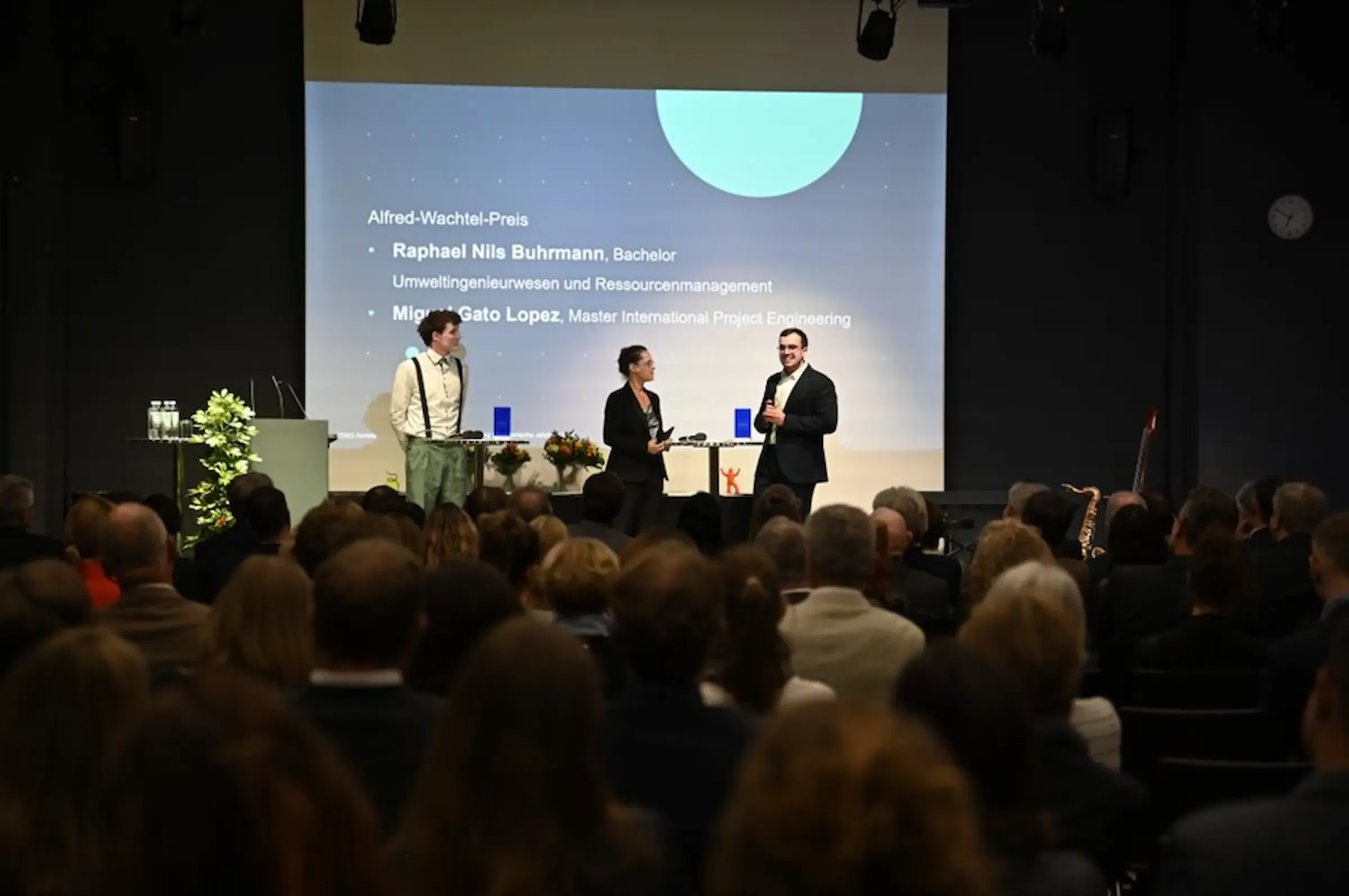Titelbild zeigt zwei Preisträger und die Moderatorin auf der Bühne